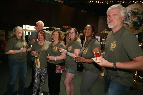 Group of people in matching green shirts socializing at an event, holding drinks and smiling.